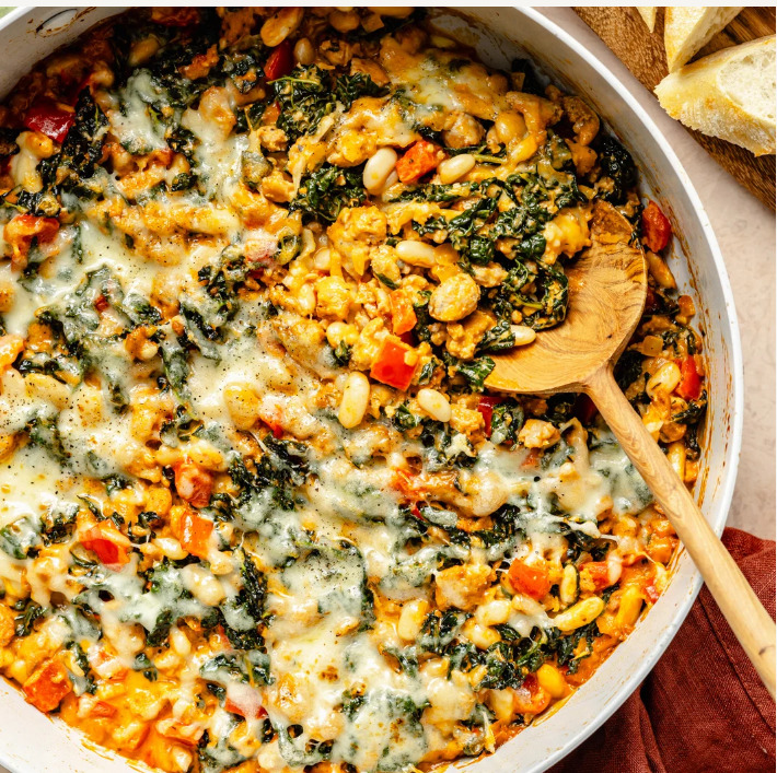 Baked white bean casserole with melted cheese, kale, and vegetables in a skillet