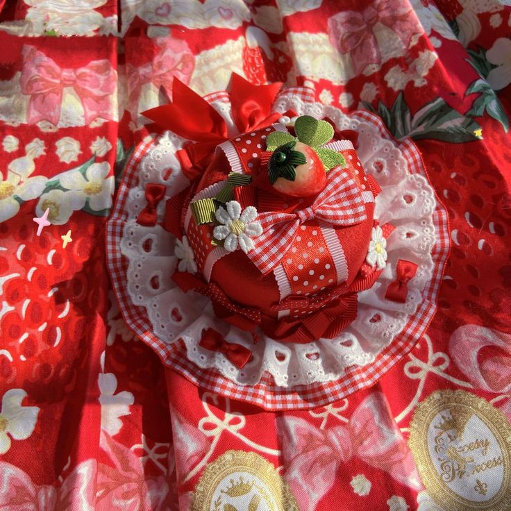 Red strawberry-themed fascinator hat with lace, bows, and flower details on patterned fabric