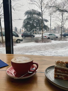 Red latte cup and layered cake on a cafe table beside a window with a snowy street outside