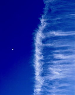 Deep blue sky with diagonal white wispy clouds and a small crescent moon