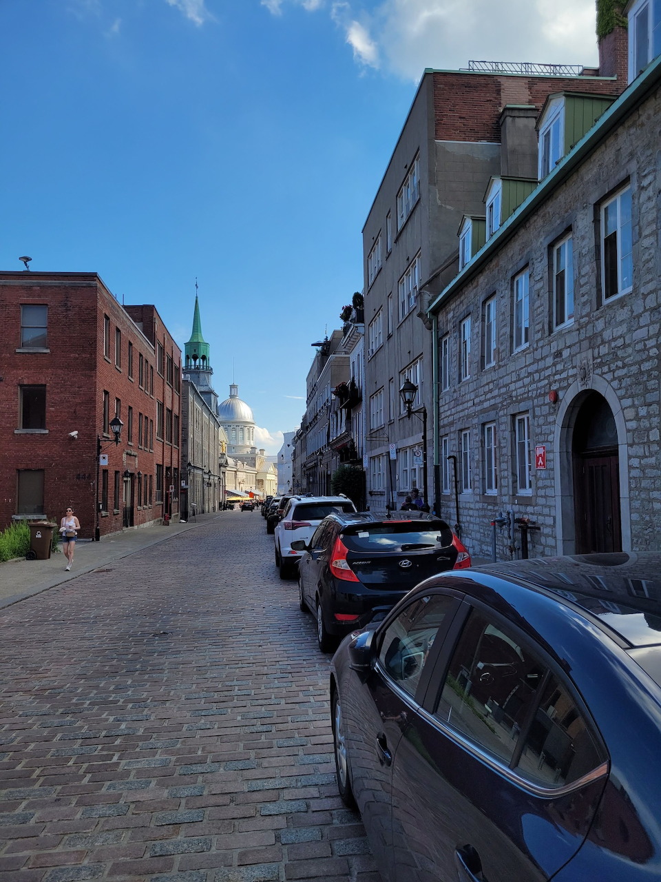 Cobblestone Rue Saint-Paul in Old Montreal with historic buildings, parked cars, and a church steeple in the background