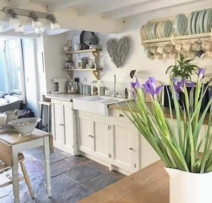 Bright white cottage kitchen with purple iris flowers on wooden table, open shelving and rustic decor