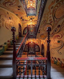 Ornate interior staircase with swirling painted walls, stained glass, and carved wooden railings