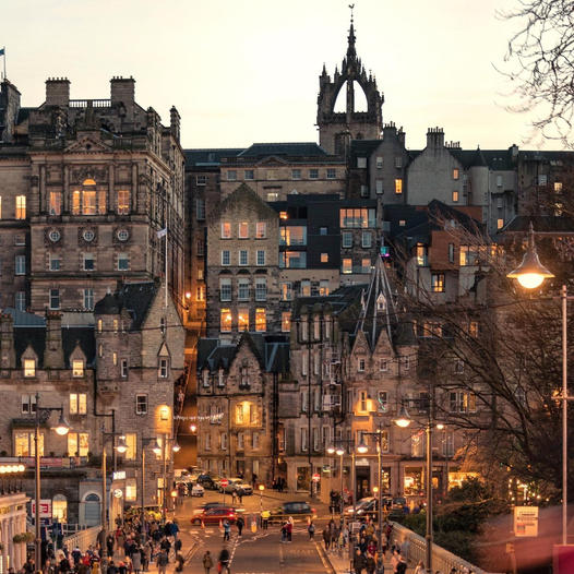 Edinburgh Old Town architecture at dusk with lit windows and church spire against cloudy sky