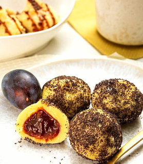 Popy seed-coated plum dumplings on a white plate with one cut open showing plum filling