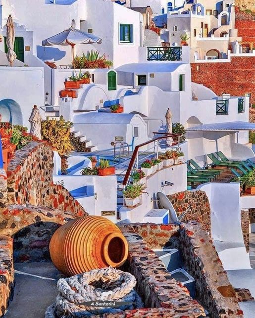 Sunlit white buildings with blue accents and clay pots in a Greek island village