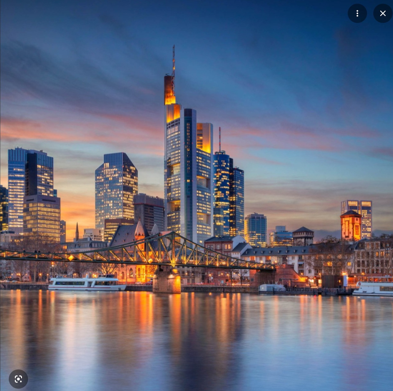 Frankfurt city skyline at sunset with illuminated skyscrapers reflected in river water
