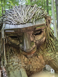 Close-up of wooden troll face sculpture with stick hair and woven beard in forest