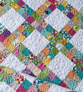 Colorful patchwork quilt with white diamond blocks and ornate stitching surrounded by vibrant patterned fabric squares