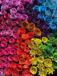 Colorful handmade paper roses arranged in rainbow gradient from pink to blue to yellow and green
