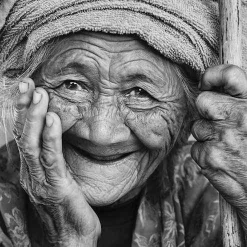 Black and white portrait of smiling elderly woman with wrinkled face and head covering