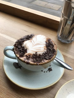 Cup of latte with leaf foam art and chocolate shavings on a saucer