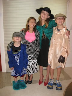 Four young girls wearing oversized adult clothes, hats, and shoes posing together indoors