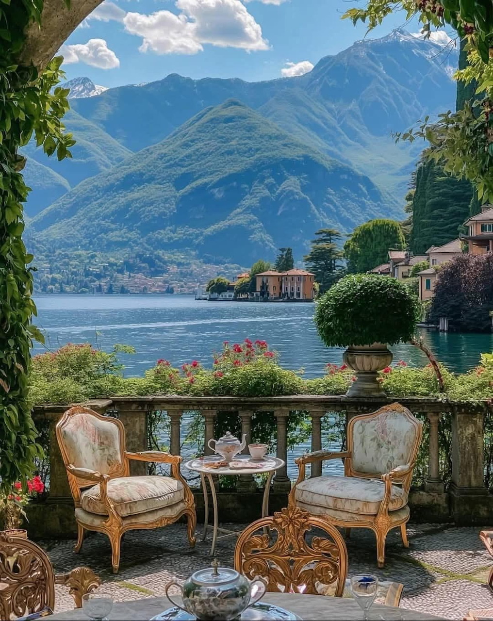 Scenic terrace with vintage chairs overlooking Lake Como, mountains, and villa through foliage frame