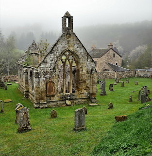 Ruined stone church with Gothic windows surrounded by gravestones in a misty Scottish graveyard
