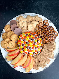 Dessert platter with colorful candy-topped dip, cookies, pretzels, apple slices, and chocolate treats arranged on white plate