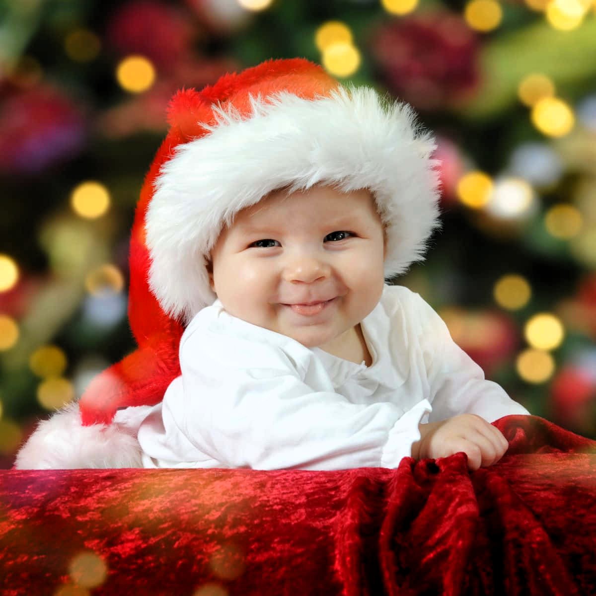 Happy baby in Santa hat smiling at camera with Christmas tree background