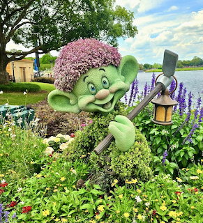 Topiary sculpture of Dopey holding lantern in flower garden with lake background