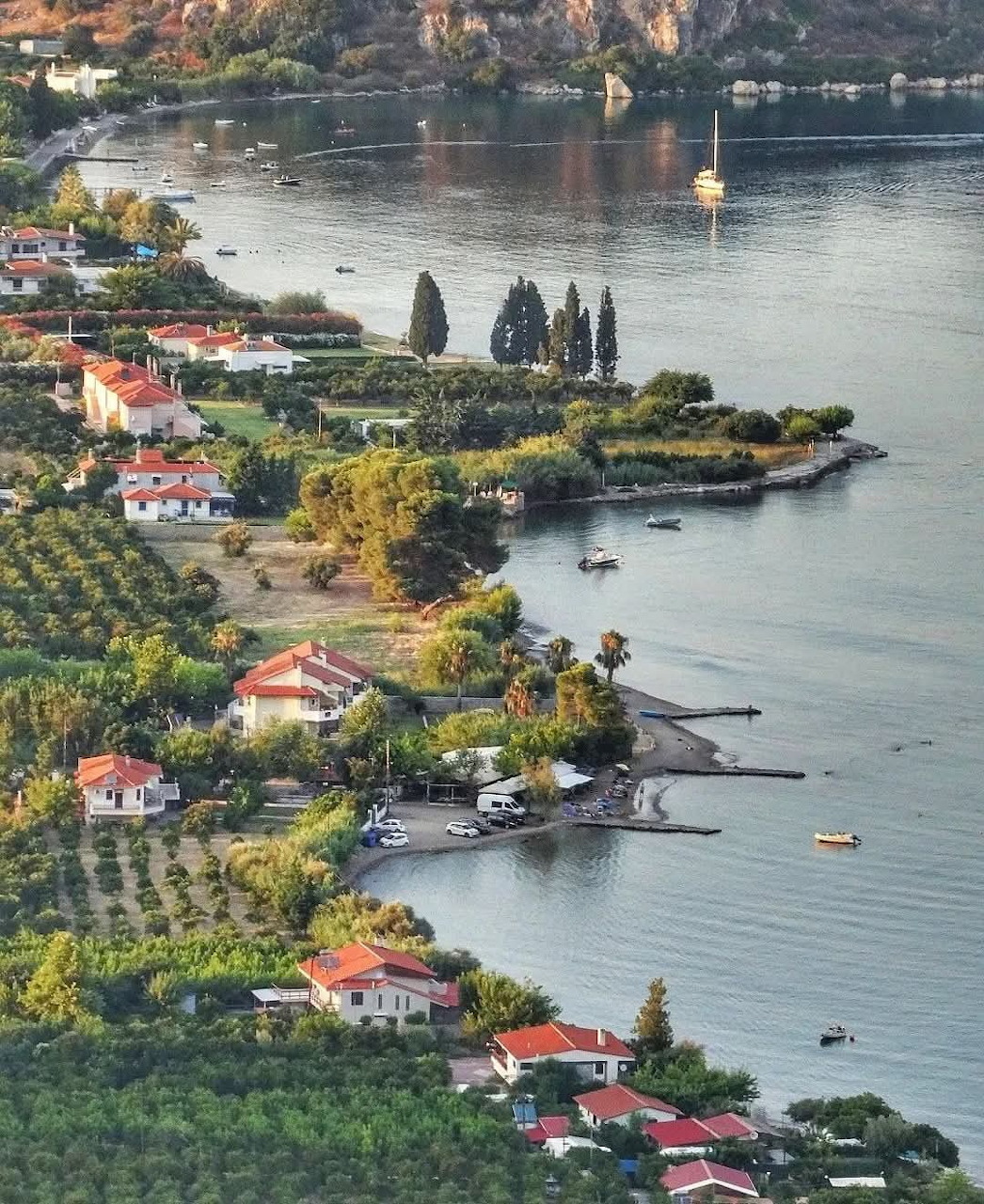 Aerial view of a Greek coastal village with red-roofed houses nestled among green trees along a calm bay