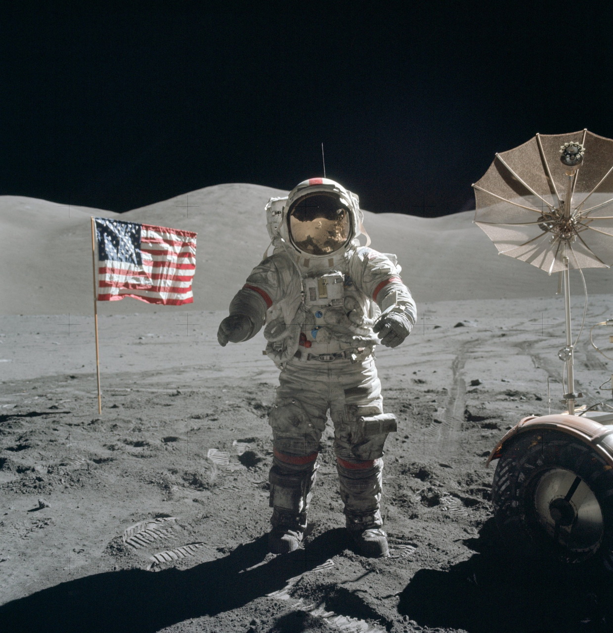 Astronaut in white spacesuit standing on gray moon surface beside American flag