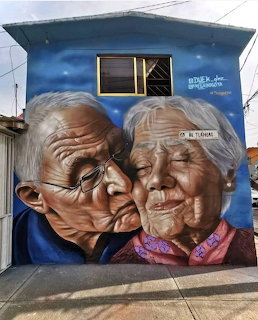 Realistic street mural of an elderly couple embracing painted on the side of a blue building