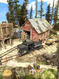 Model train diorama with steam locomotive, red mining building, coal tipple, and evergreen trees