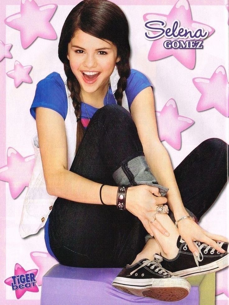 Selena Gomez sitting and smiling on a pink star background