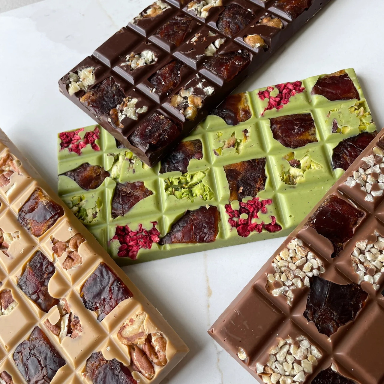 Assorted decorated chocolate bars with nuts and dried fruit toppings on white plates