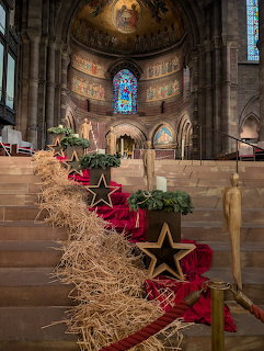 Church interior with Christmas decorations, straw bales with gold stars along red carpet leading to decorated tree and altar