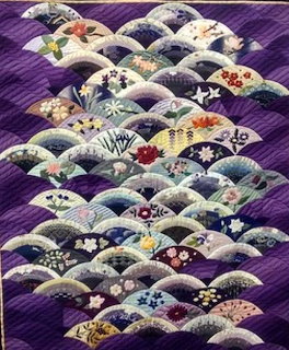 Quilt with overlapping Japanese fan pattern blocks on purple background, decorated with floral motifs