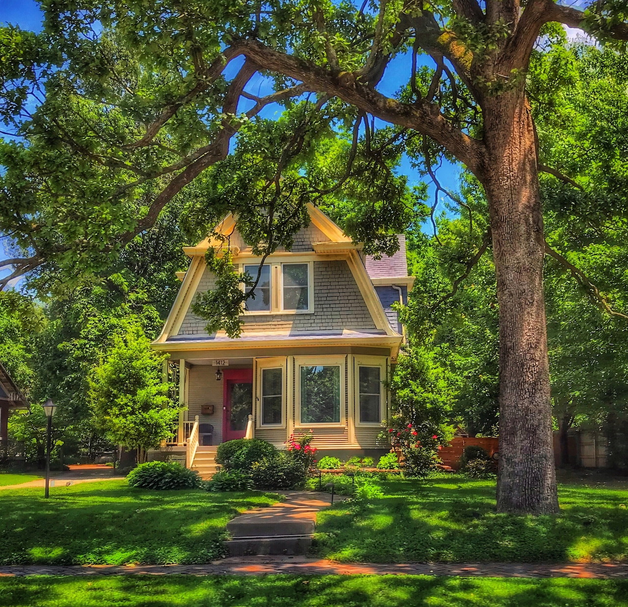 Yellow Victorian cottage with wraparound porch beneath large oak tree on green lawn