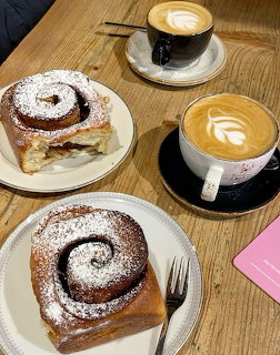 Two cinnamon rolls with powdered sugar and two cappuccinos with latte art on wooden table