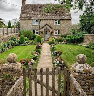 Stone cottage with formal garden, wooden gate, flower beds, and lawn path under cloudy sky