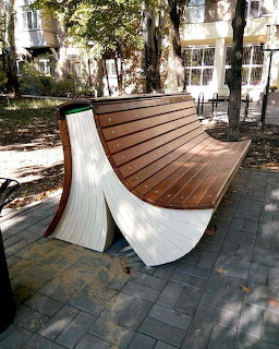 Curved wooden bench on a paved path in a shaded outdoor courtyard