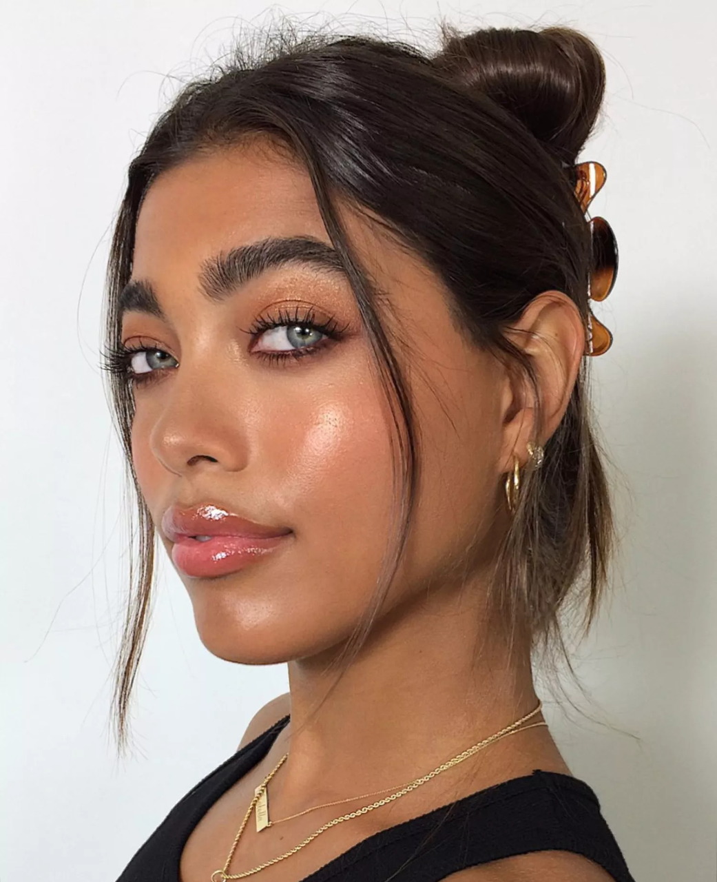 Young woman with dark hair bun, glowing skin, subtle makeup, gold hoop earrings and layered necklace
