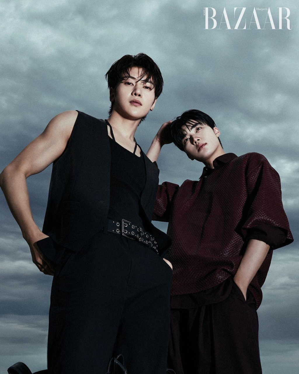Two young men in black fashion attire pose for Harper's Bazaar magazine editorial with cloudy sky background