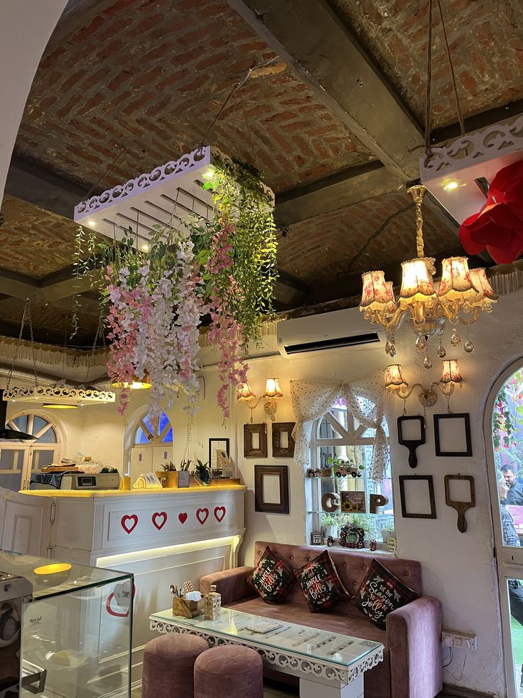 Cozy cafe interior with hanging pink flowers, chandelier, white ornate walls, and velvet sofa seating