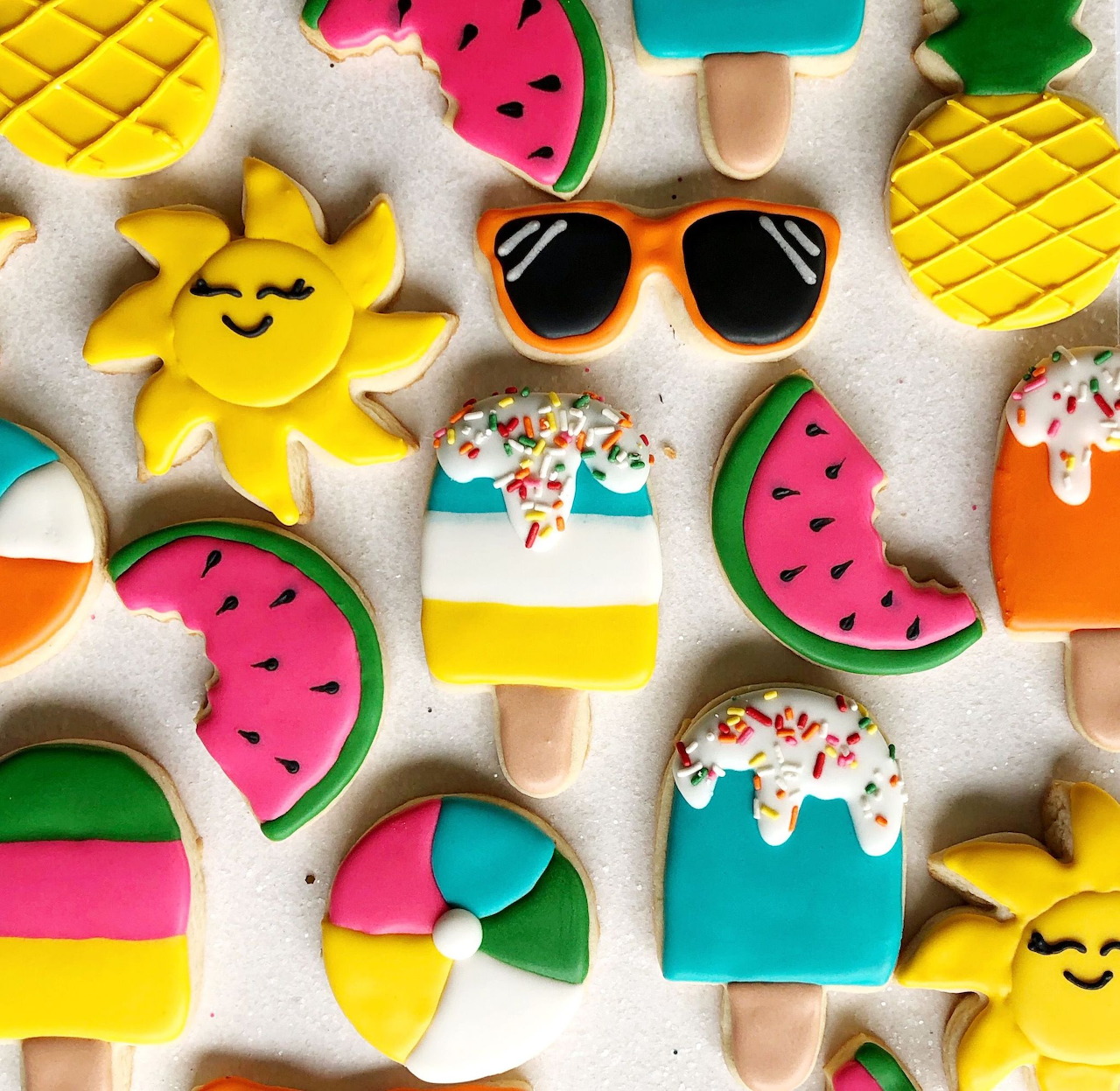 Assorted summer-themed decorated cookies including popsicles, watermelon, sunglasses, and beach balls on white background