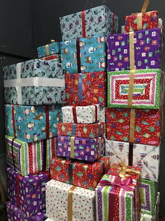 Large stack of colorful wrapped Christmas gifts with festive paper patterns, ribbons, and bows