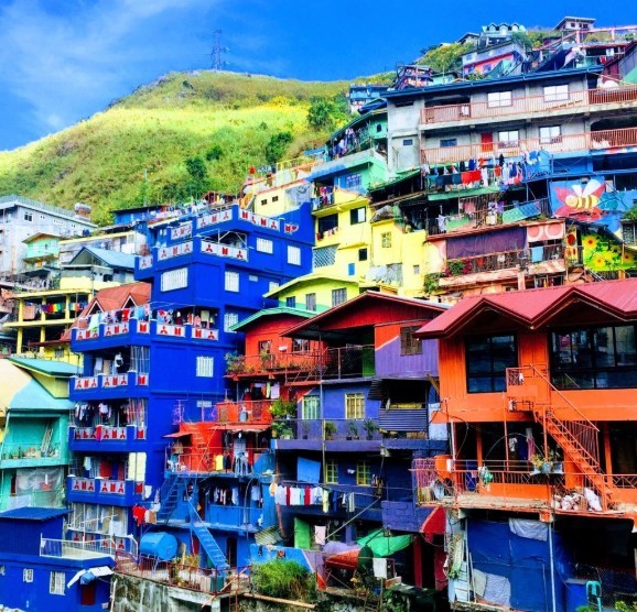 Colorful houses stacked on a hillside with green grass and blue sky