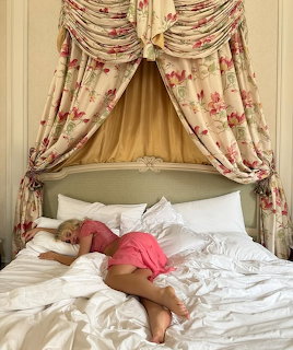 Woman in pink clothing lying on white bed under decorative floral curtain canopy