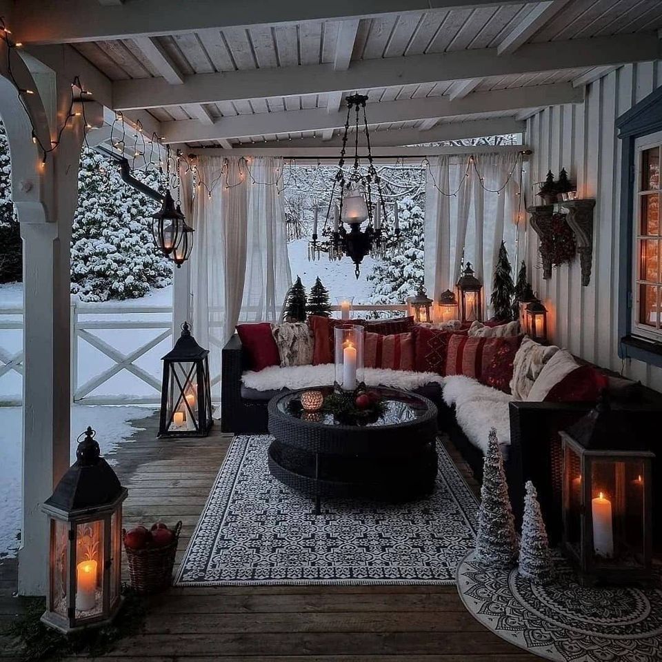 Cozy covered porch with candles, pillows, curtains, and snowy trees outside