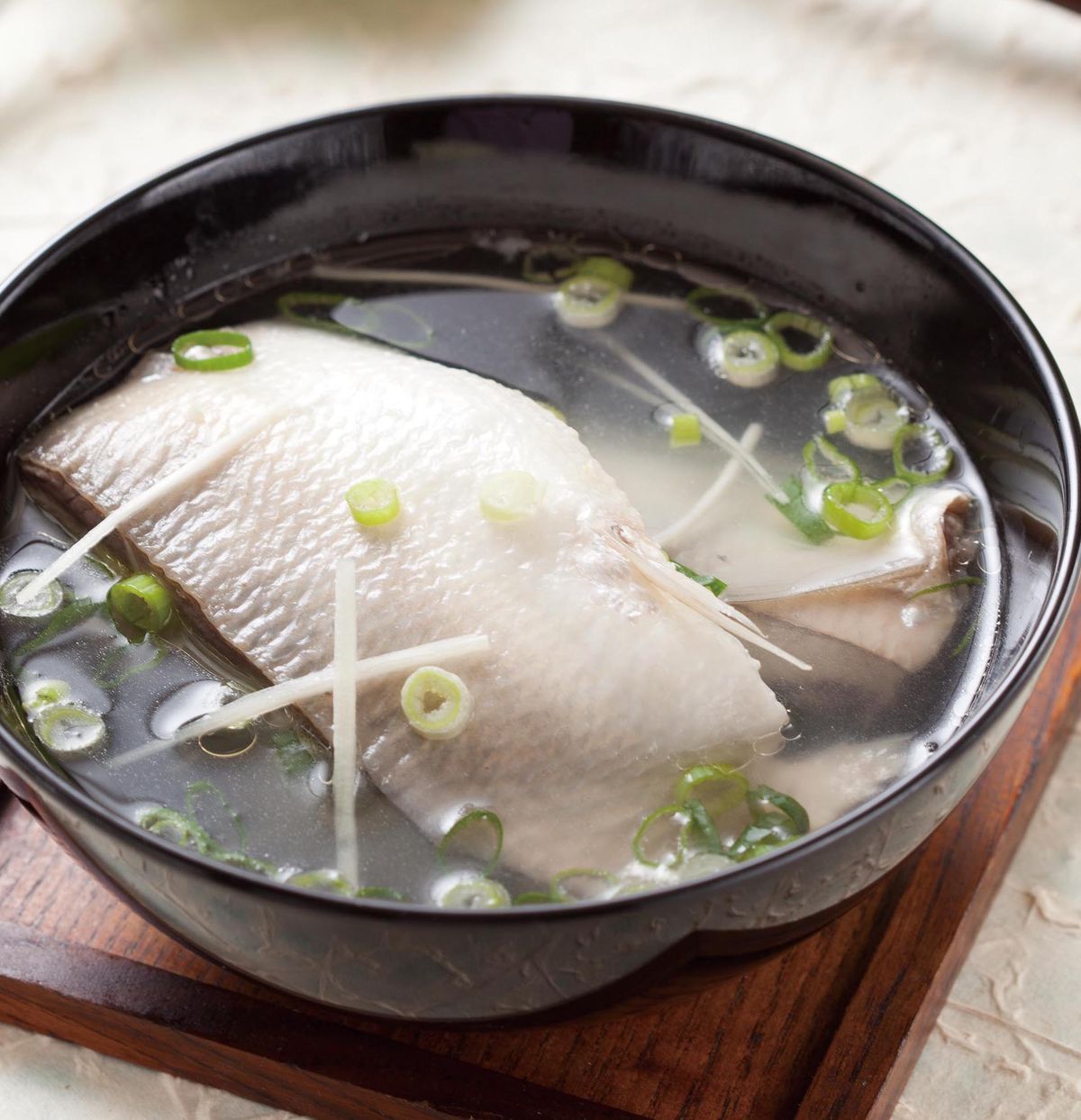 Black bowl of clear fish soup with white fish slices, bean sprouts, and scallions