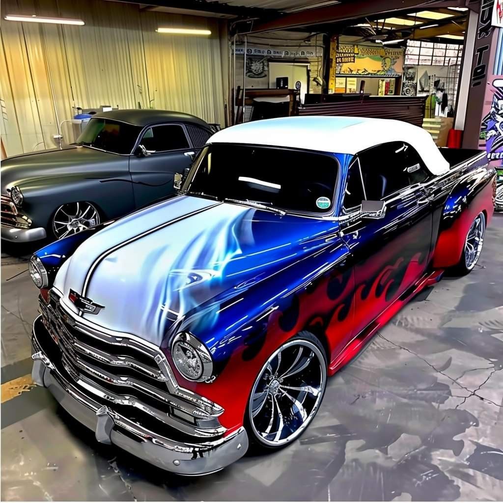 Blue vintage custom pickup truck with chrome grille and flame graphics in a garage