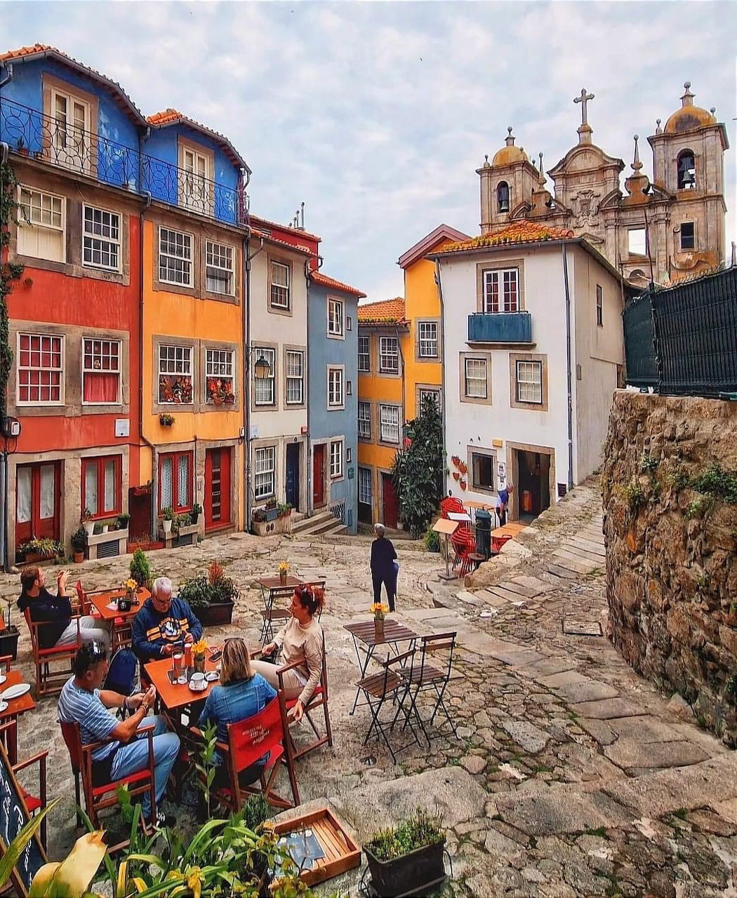 Narrow cobblestone street lined with colorful buildings and people dining at outdoor café tables in Porto, Portugal