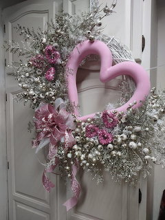Pink heart-shaped wreath with silver branches, white berries, and pink floral ribbon on a white cabinet door