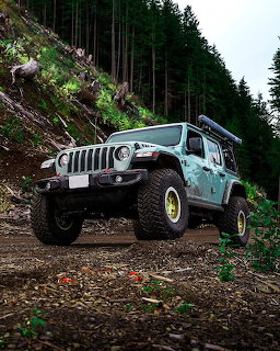 Modified teal Jeep Wrangler driving on a muddy off-road trail in a forested hillside