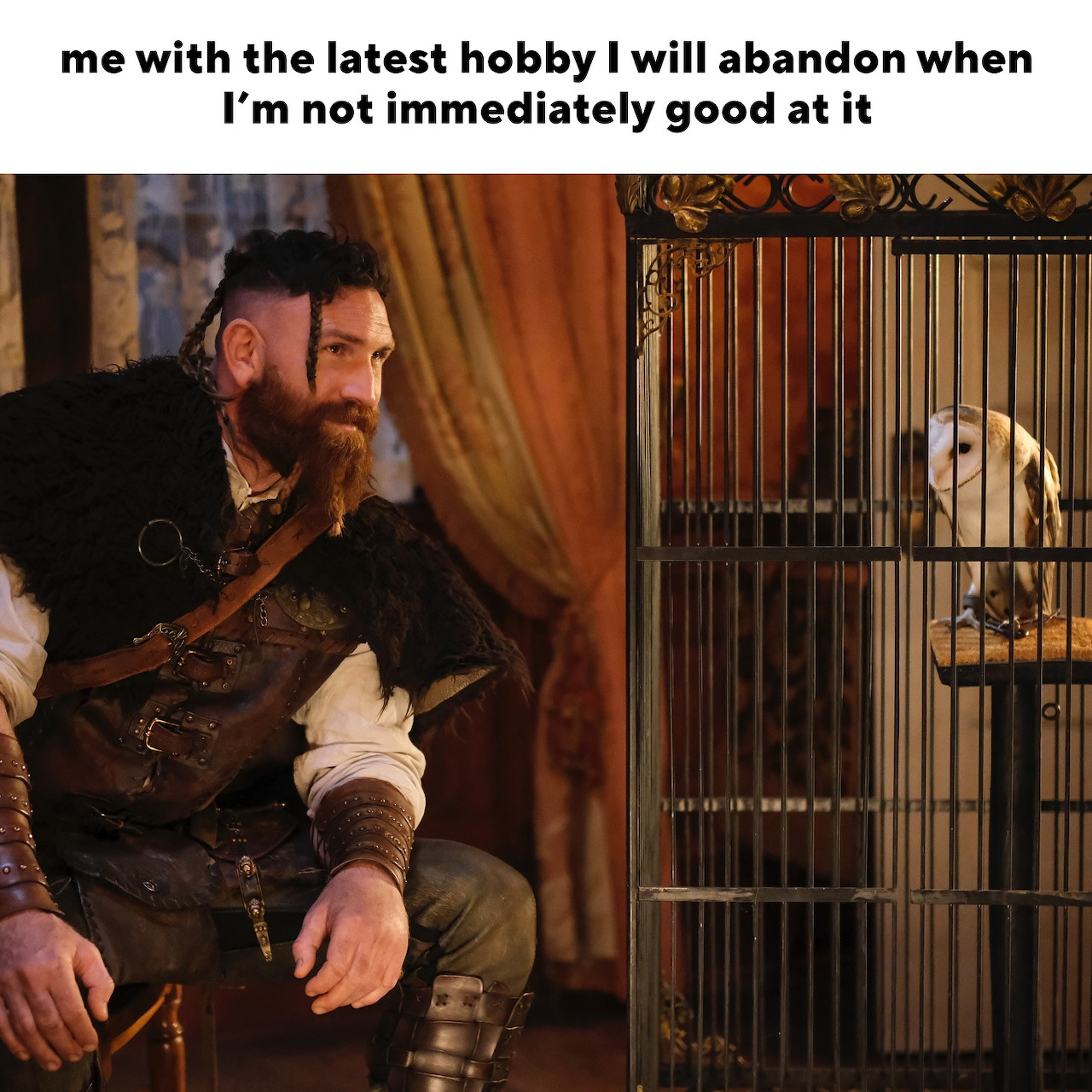 Bearded man in historical costume holding brown owl with caged white owl nearby