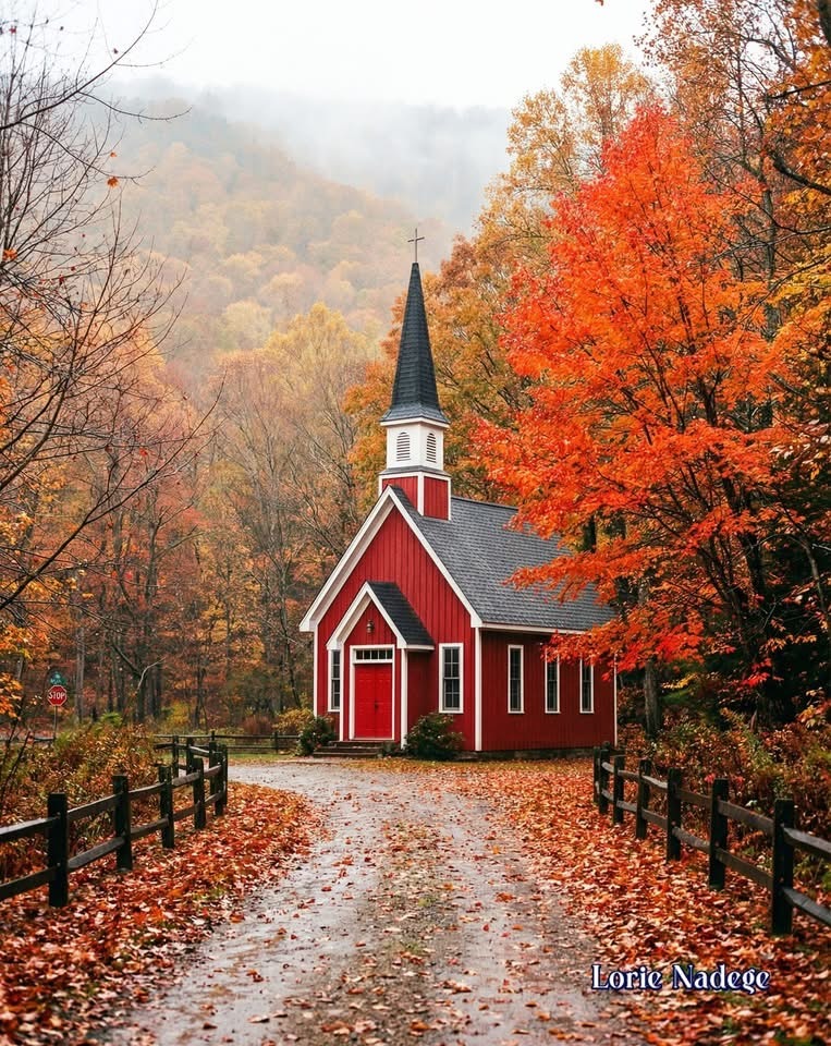 Red church at the end of a leaf-covered path with orange autumn trees and misty hills