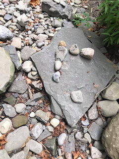 Flat gray slate stone with small pebbles arranged on top, surrounded by gravel